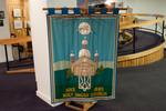 This processional banner was made by parishioners in 1985. Their names are embroidered on the bottom corner: Betty Marmulak, Mary Pronko, Kaye Melenchuk, Lydia Tatanish, Helen MacLean. It was donated to the Holy Ghost parish in memory of Walter Marmulak, by his family. In the entrance to the Holy Ghost Ukrainian Catholic Church, a table is laid with prayer books, church bulletins and other items.